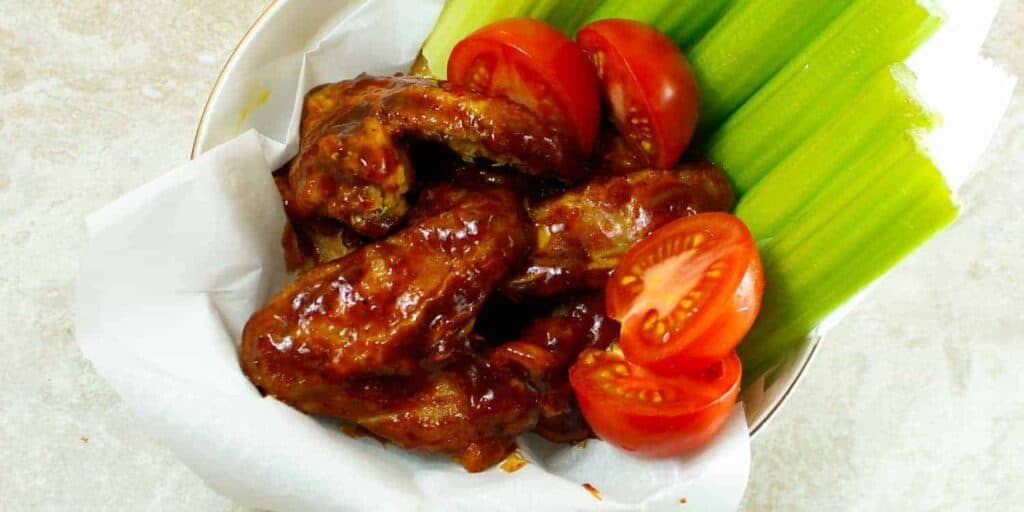 bbq chicken wings in a bowl with celery and tomato