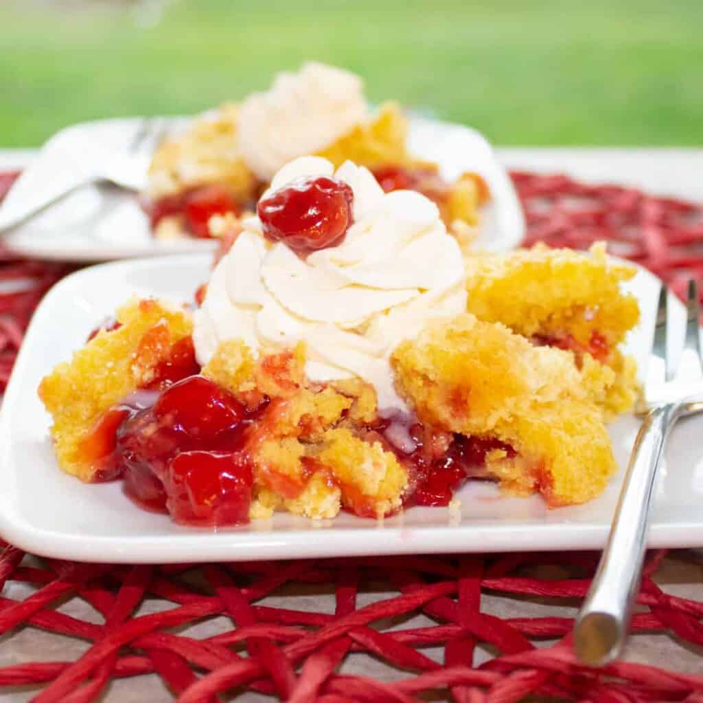 3 ingredient cherry dump cake on a plate with whipped cream
