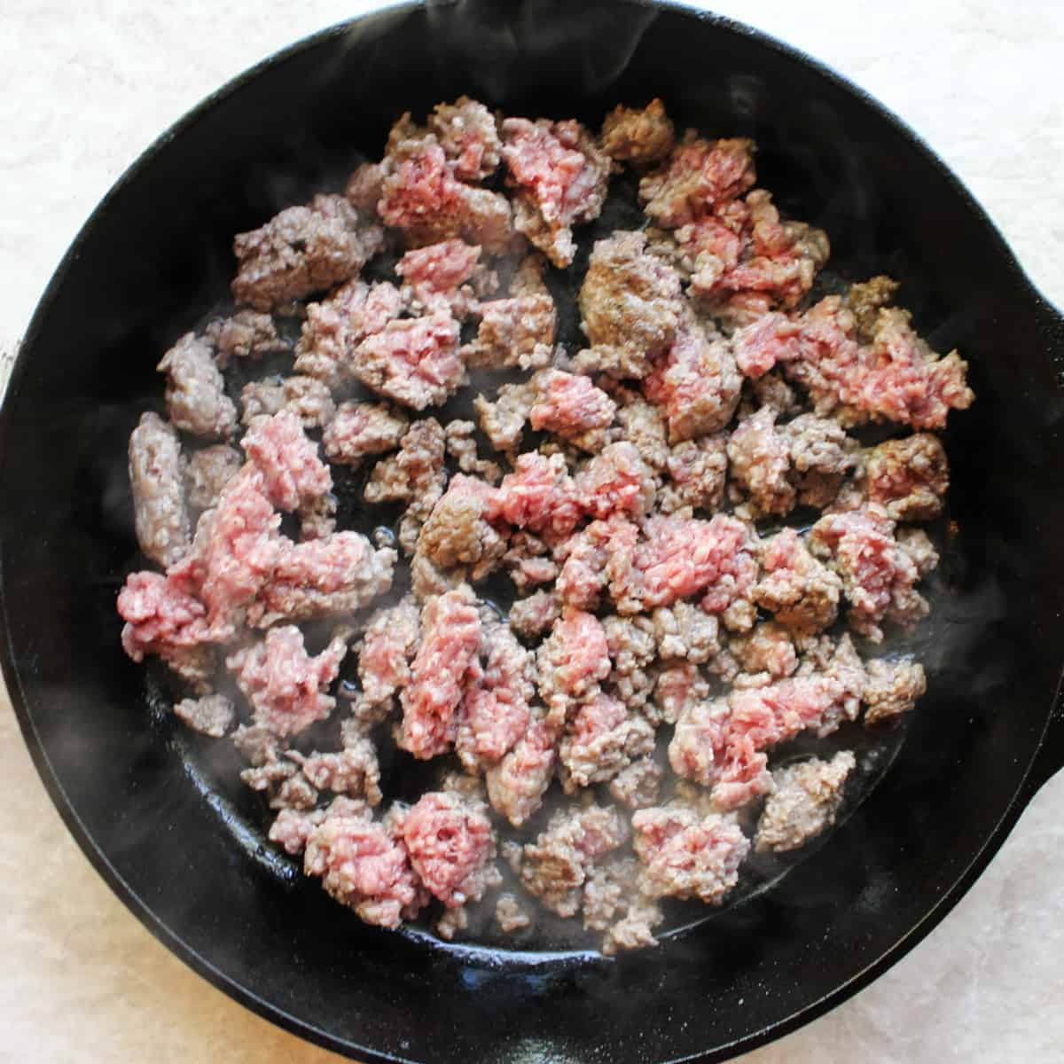 ground beef browning in a cast iron skillet